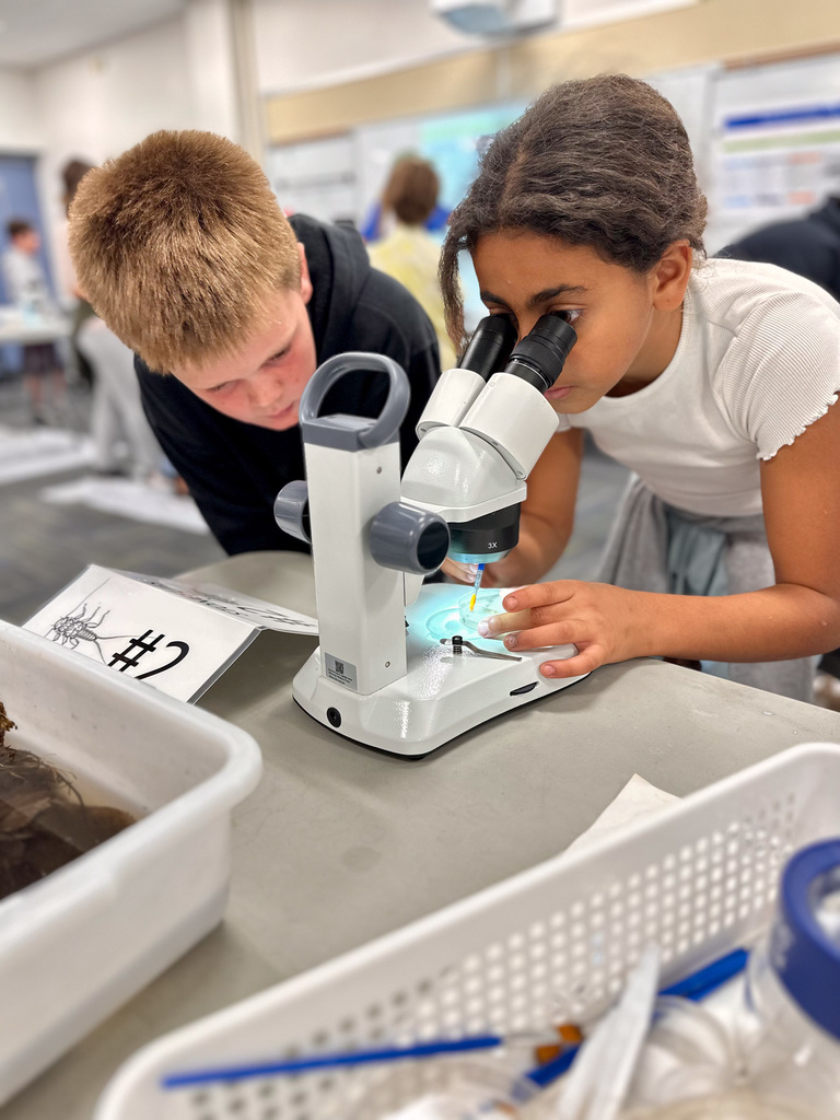 Two students using a microscope at a science station labeled '#2'.