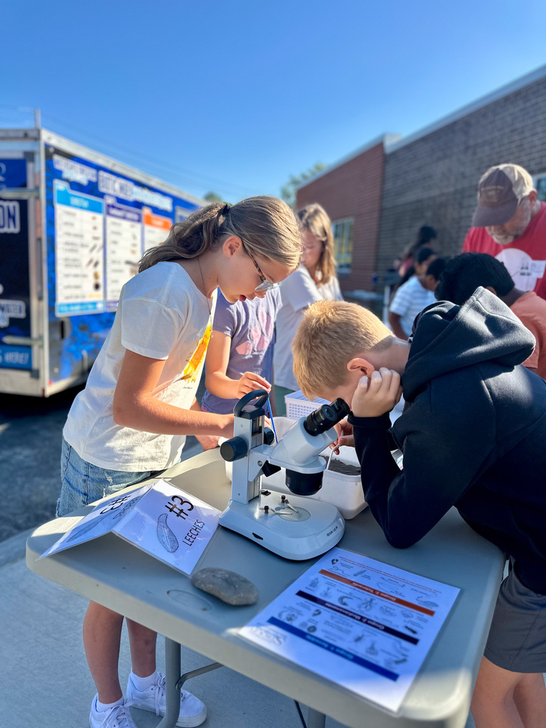Children using microscopes at an outdoor science activity with the Stroud Water Research truck in the background.