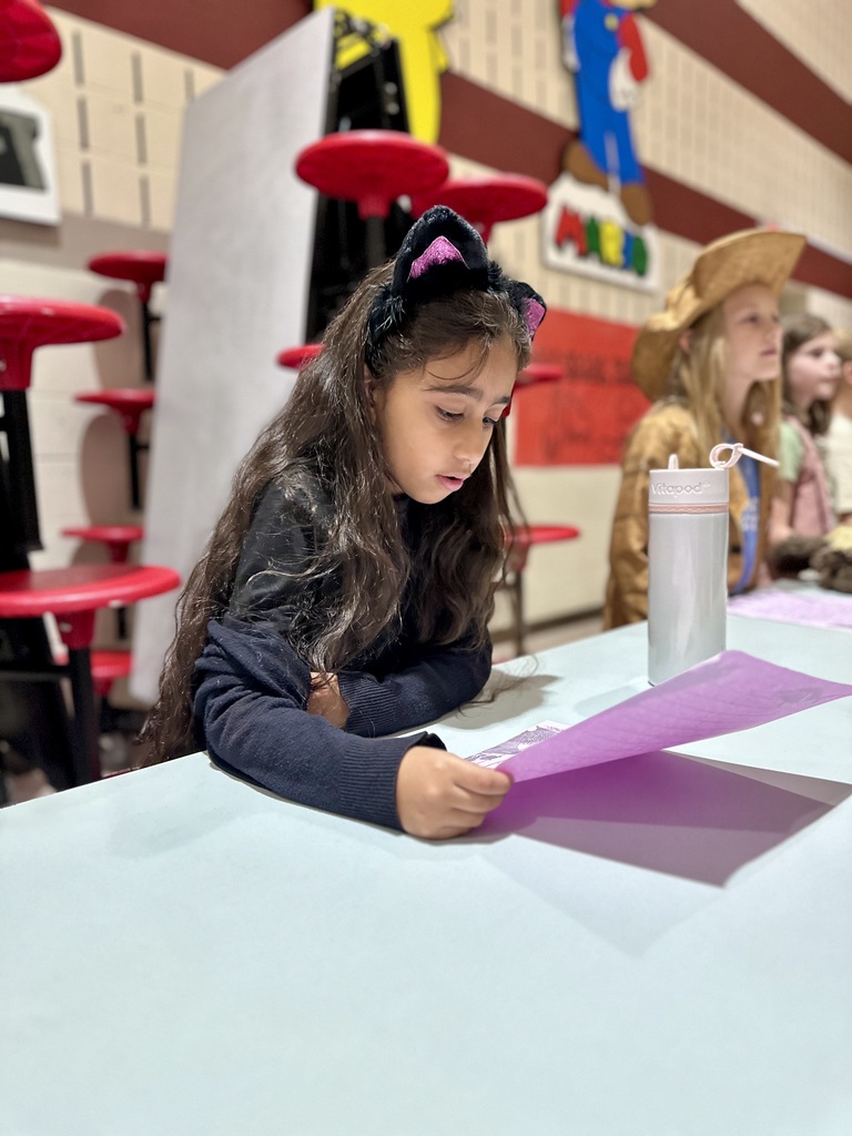 A student dressed in all black with a cat-ear headband, reads from a purple sheet of paper.