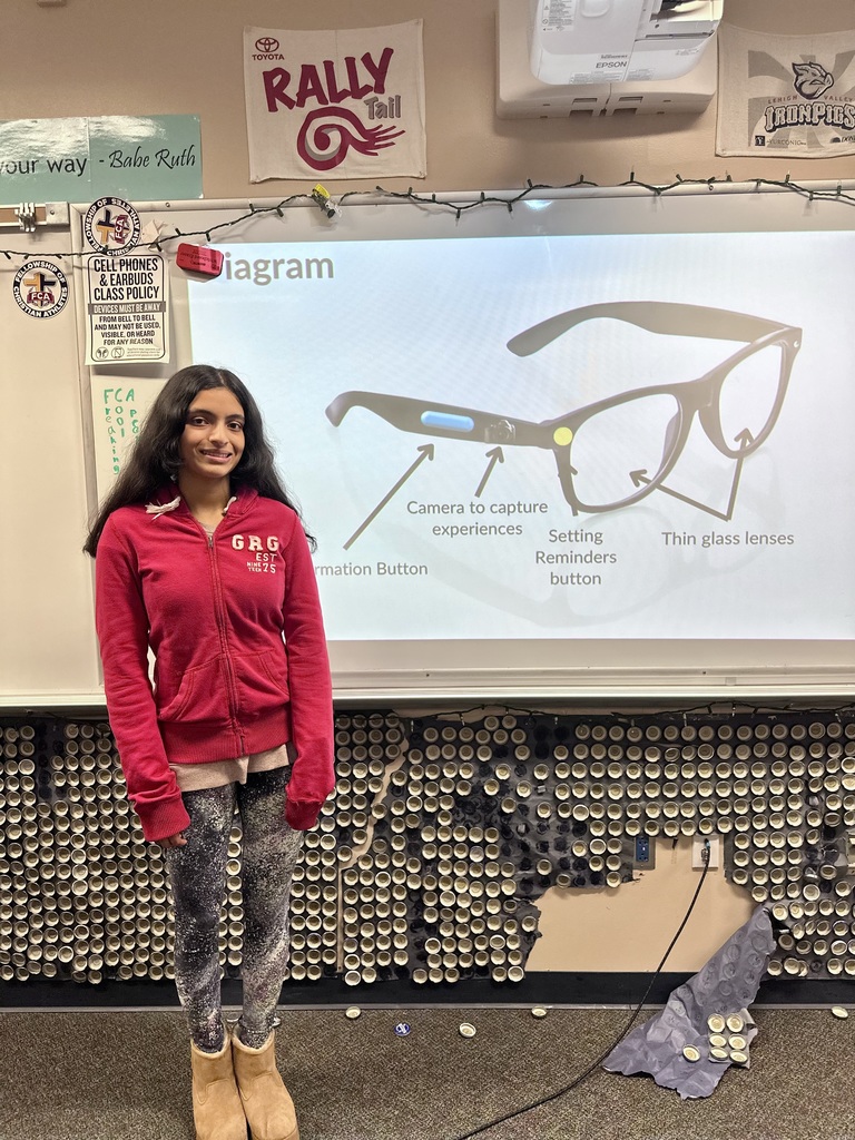 A student in a red jacket presents a Shark Tank idea for smart glasses, with a classroom screen showing a diagram of the glasses and their features.