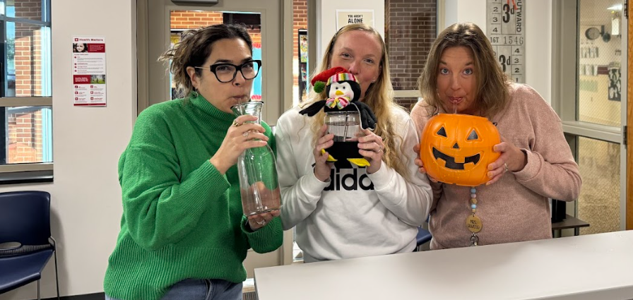 One teacher drinking from glass carafe, another drinking from a mason jar with penguin top, and another teacher drinking from trick-or-treat pumpkin bucket.