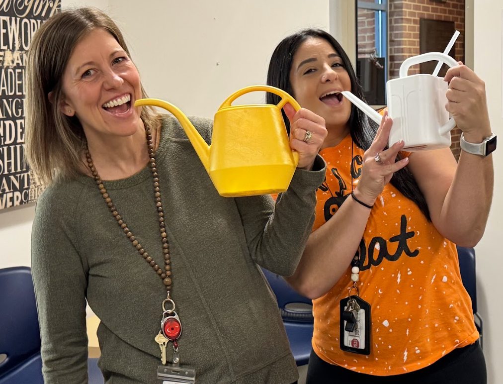 Two teachers smiling and drinking from watering cans