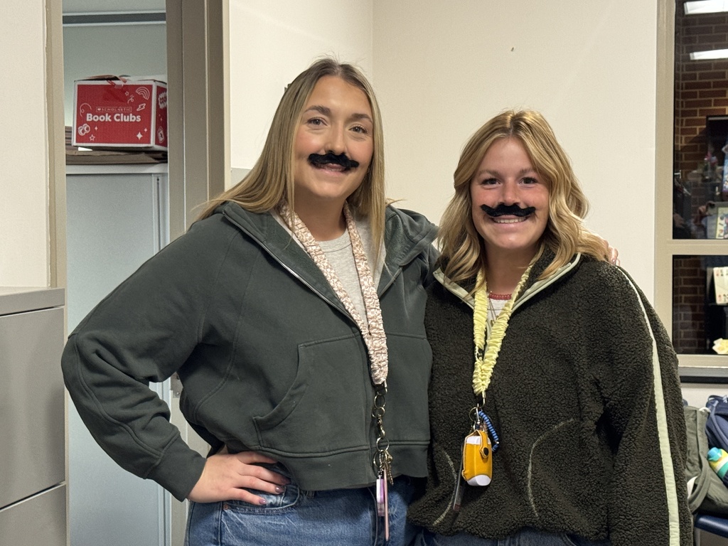 Two female teachers wearing fake mustaches and smiling
