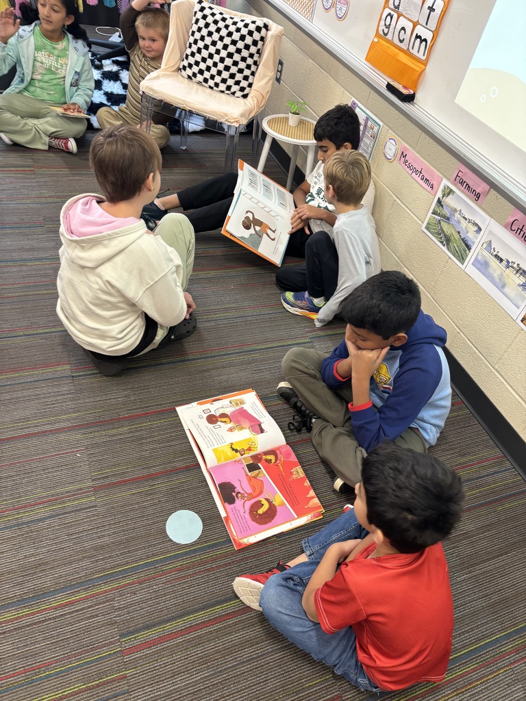 Winding Creek Elementary students in the Pages & Pals group sit on a classroom carpet reading picture books together.