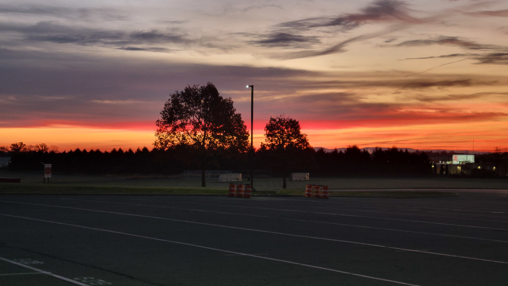 CVHS' parking lot at sunset with vibrant orange, pink, and purple hues in the sky, silhouetted trees, and a single light pole in the center.