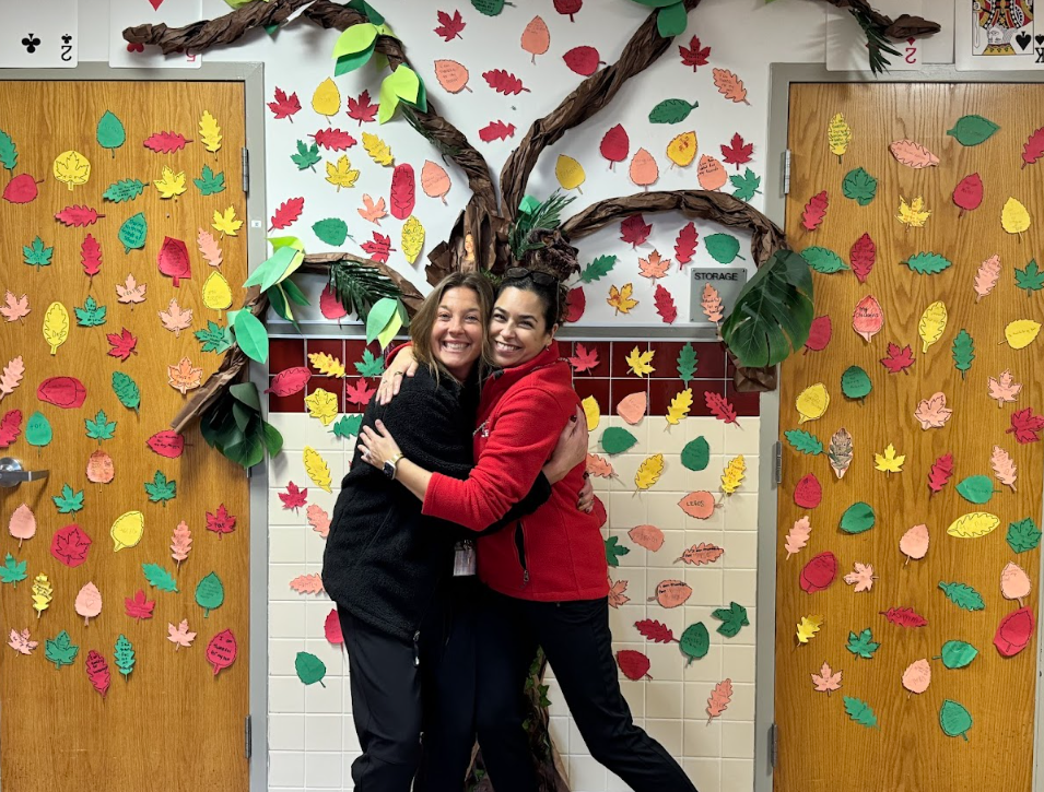 Two women hugging in front of paper Tree of Thanks