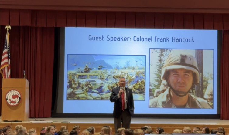 Man speaking in front of students with a picture of himself while serving active duty in Army.