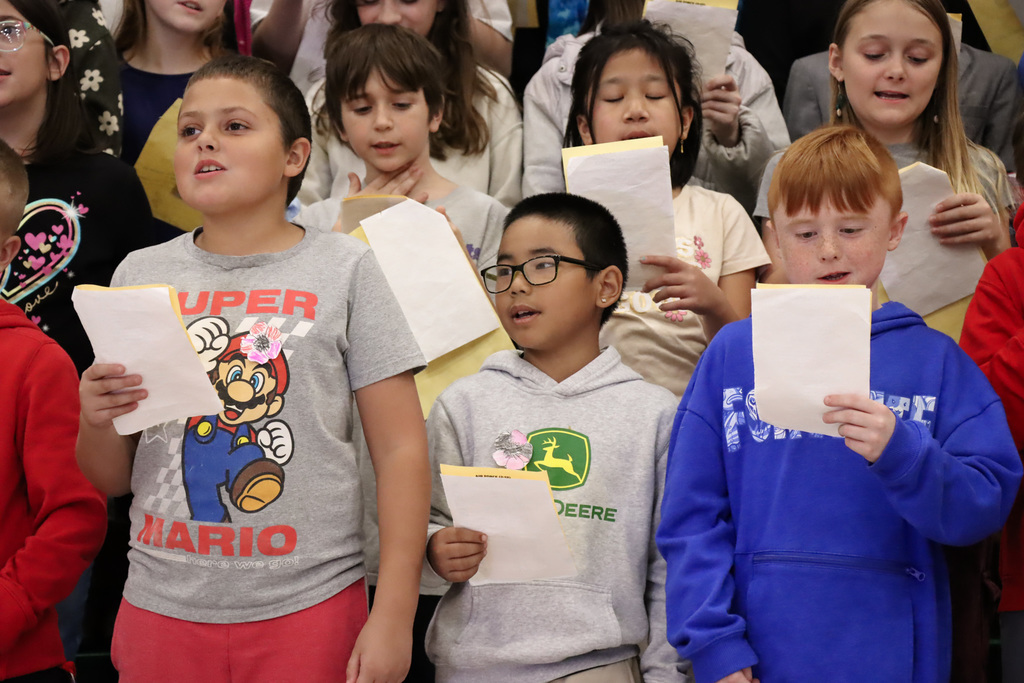 Students holding papers while singing during a Veterans Day assembly.