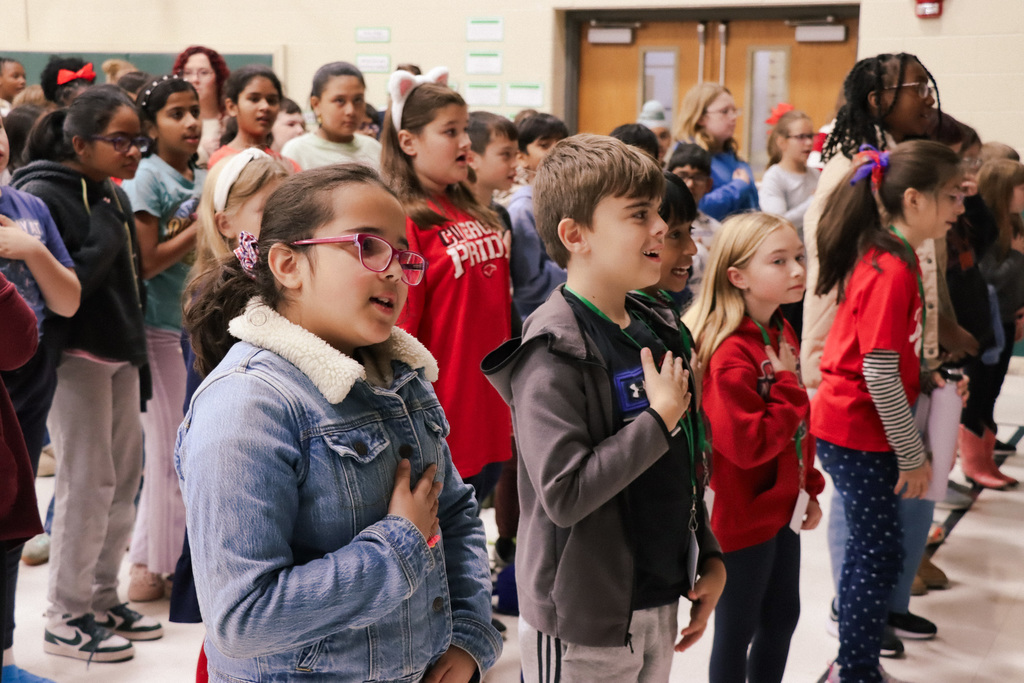 Students signing with their right hand over their heart during a veteran's day assembly.
