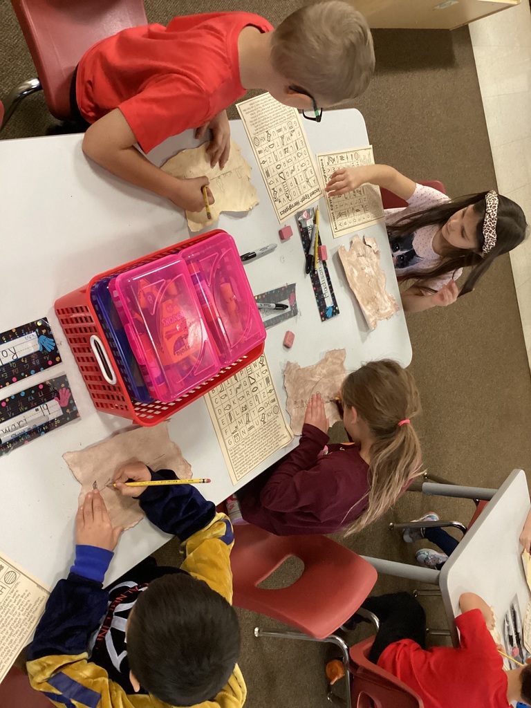 Four students sitting at a table and drawing hieroglyphics