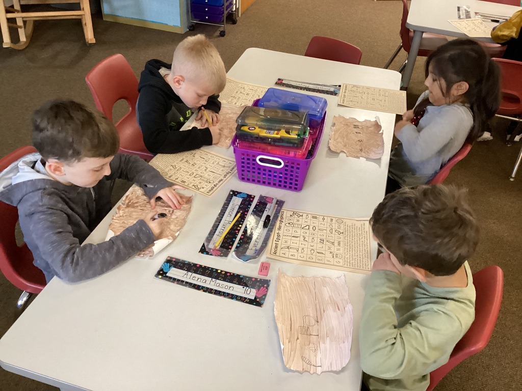 Four students sitting at a table and drawing hieroglyphics