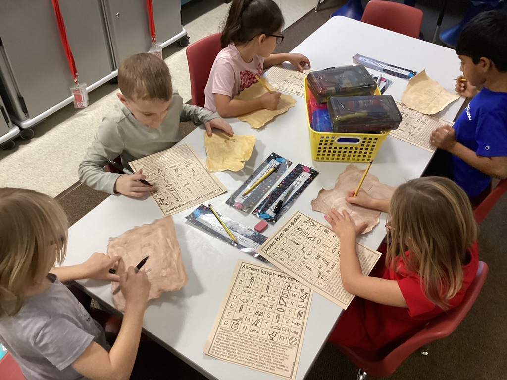Four students sitting at a table and drawing hieroglyphics