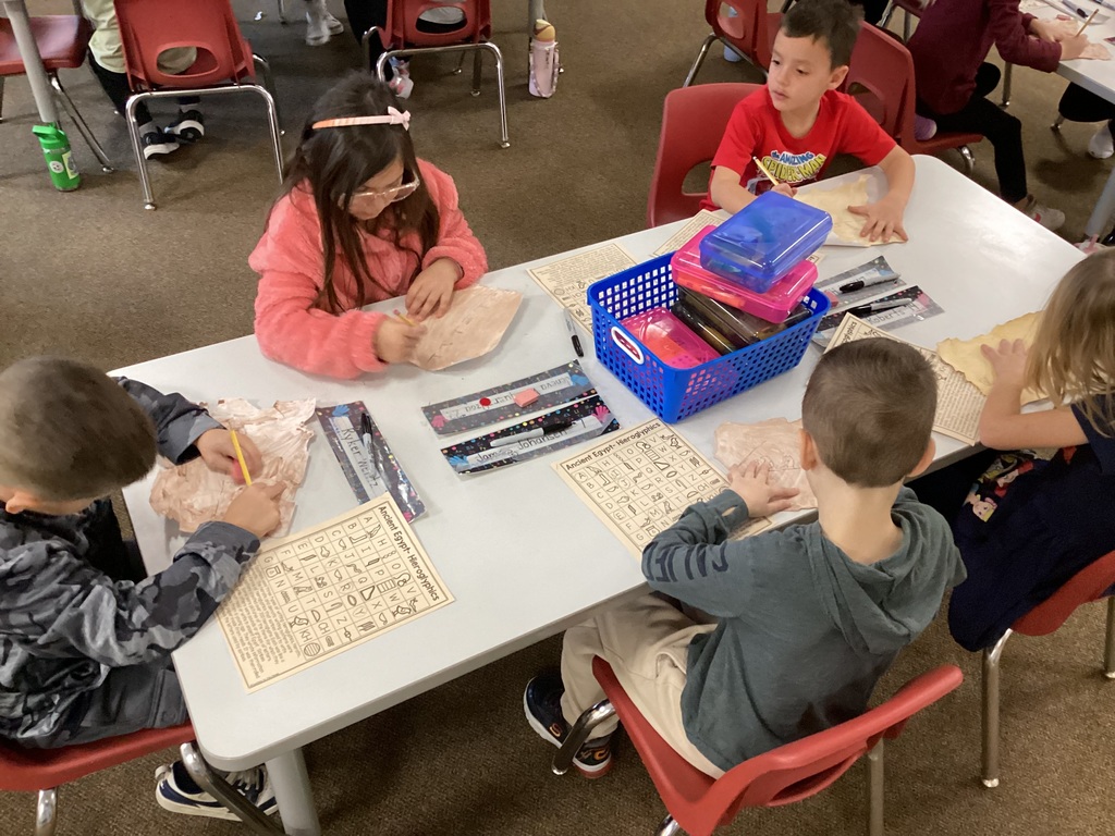 Four students sitting at a table and drawing hieroglyphics