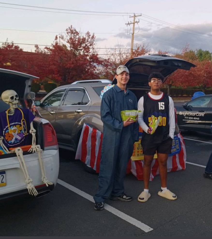 Two CVHS Golden Years Club students at a trunk-or-treat event with decorated car trunks and candy bags.