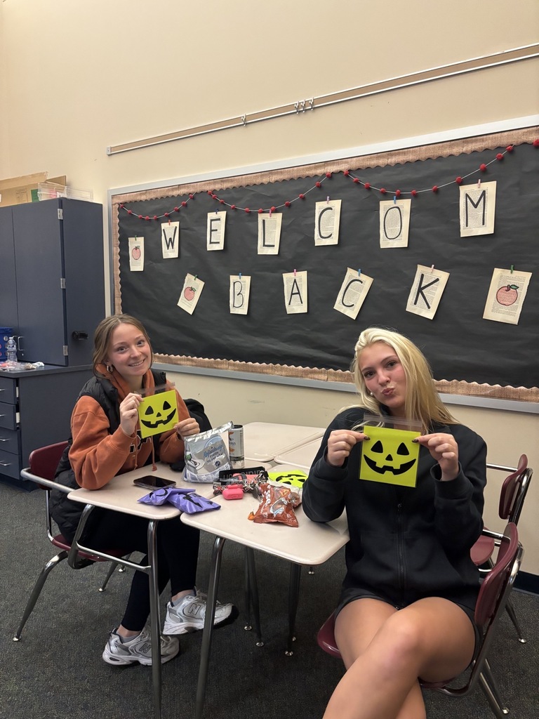CVHS Golden Years Club students sitting at a table holding bright yellow pumpkin goodie bags that they handed out to the senior community for Halloween.