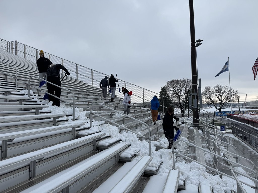Cumberland Valley Varsity Football players shovel the snow off of the bleachers at Chapman Field.