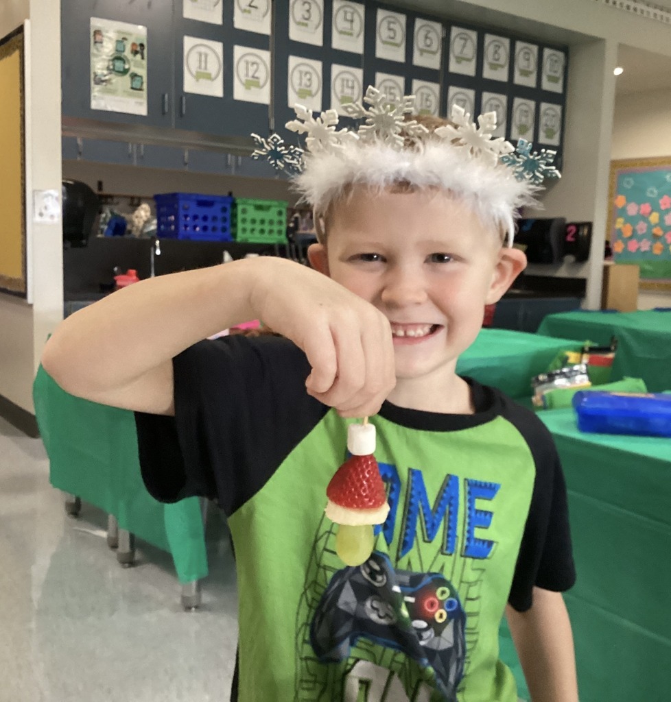 Kindergarten student at Middlesex Elementary holding a Grinch-themed snack while wearing a festive snowflake headband during Grinch Day.