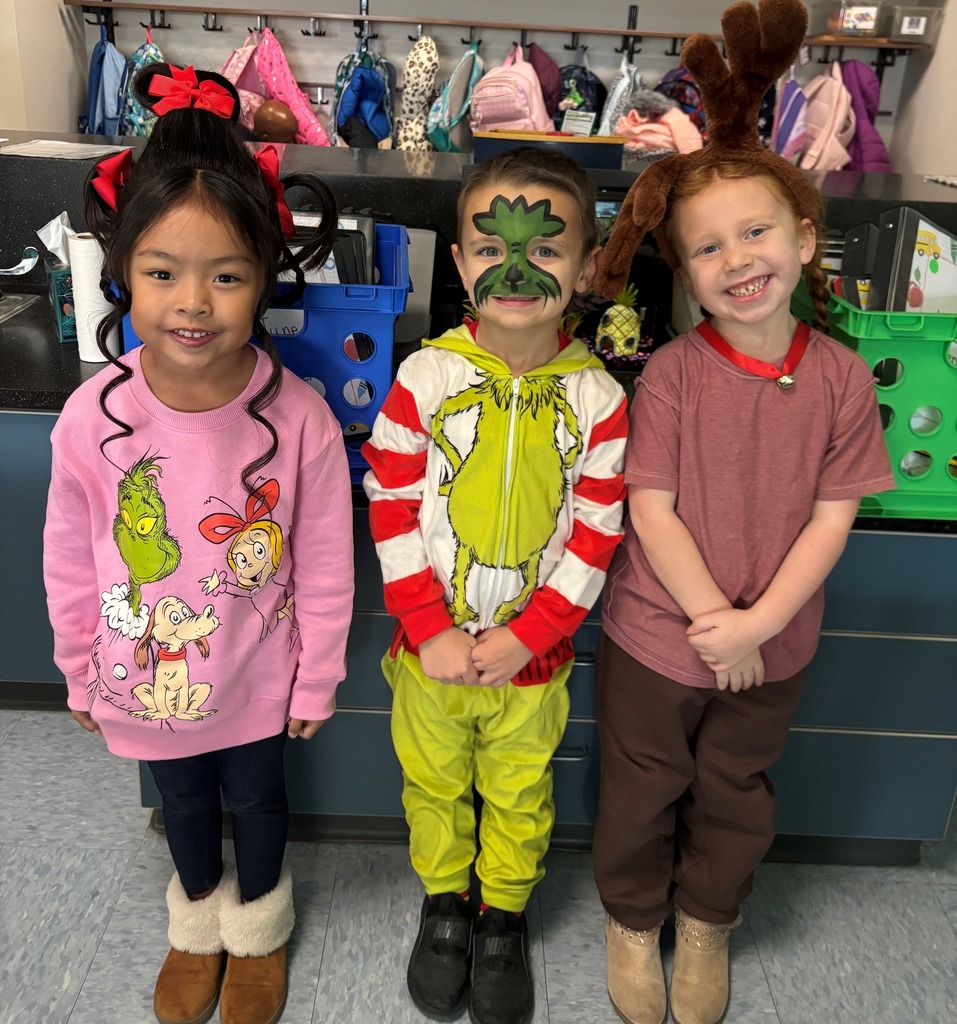 Three kindergarten students dressed in Grinch-themed outfits during Middlesex Elementary’s Grinch Day, standing in a classroom with festive hairstyles and clothing.