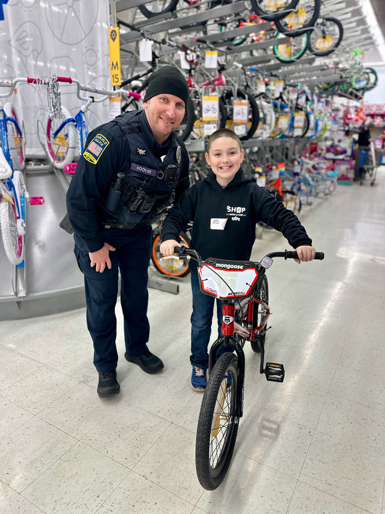 A police officer stands beside a child who is trying out a new bicycle during the 11th annual Shop with a Cop event.