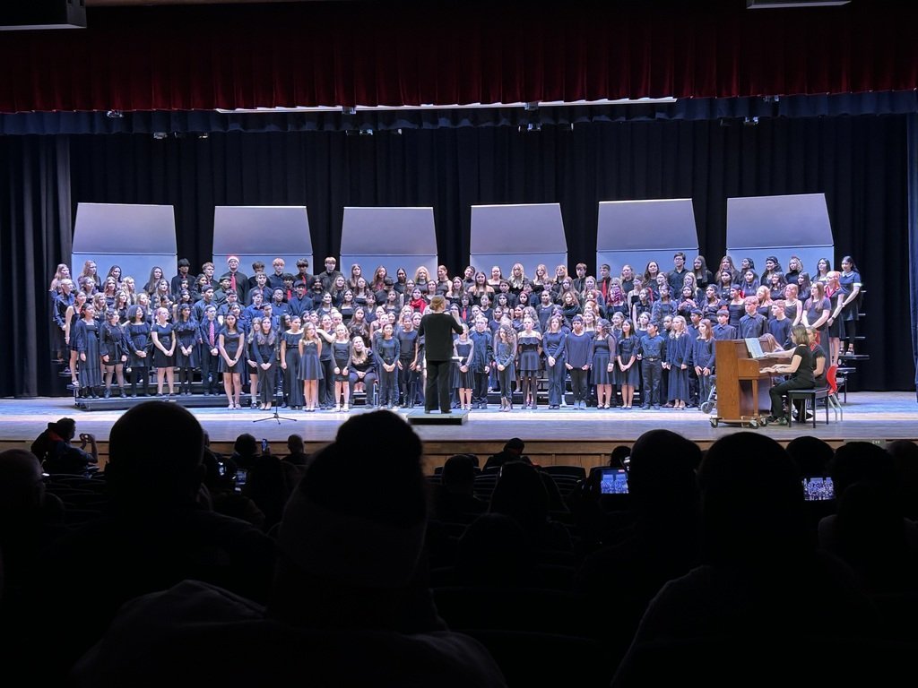 A large student choir performs on stage in Eagle View Middle School’s new auditorium during the winter concert, accompanied by a pianist.