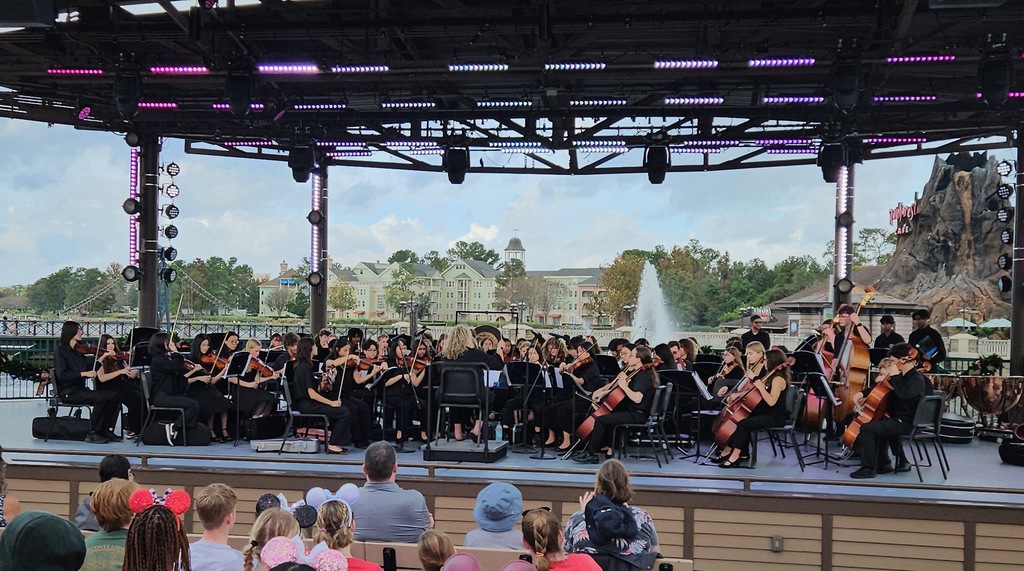 The Cumberland Valley orchestra performs on Disney’s Waterside Stage, with student string musicians playing an outdoor concert before a seated audience.