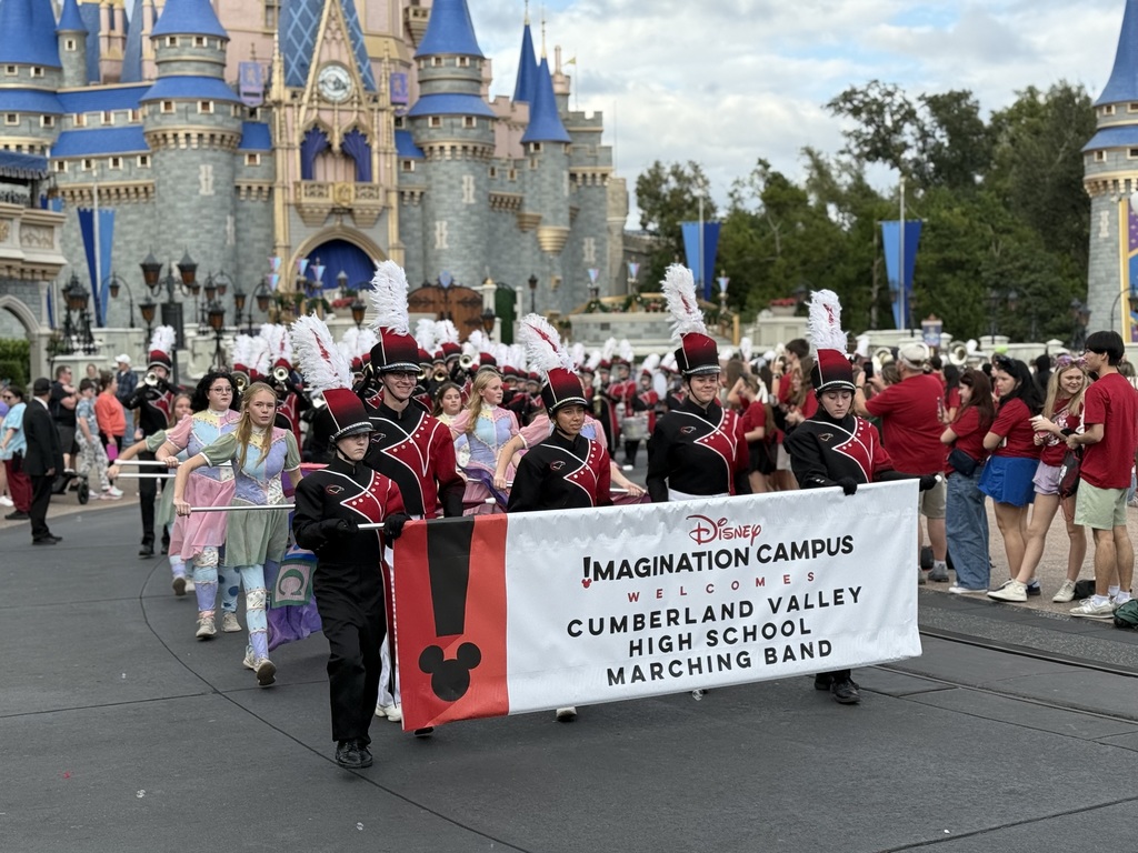 Cumberland Valley High School marching band parades down Main Street at Disney World, carrying a banner in front of Cinderella Castle.