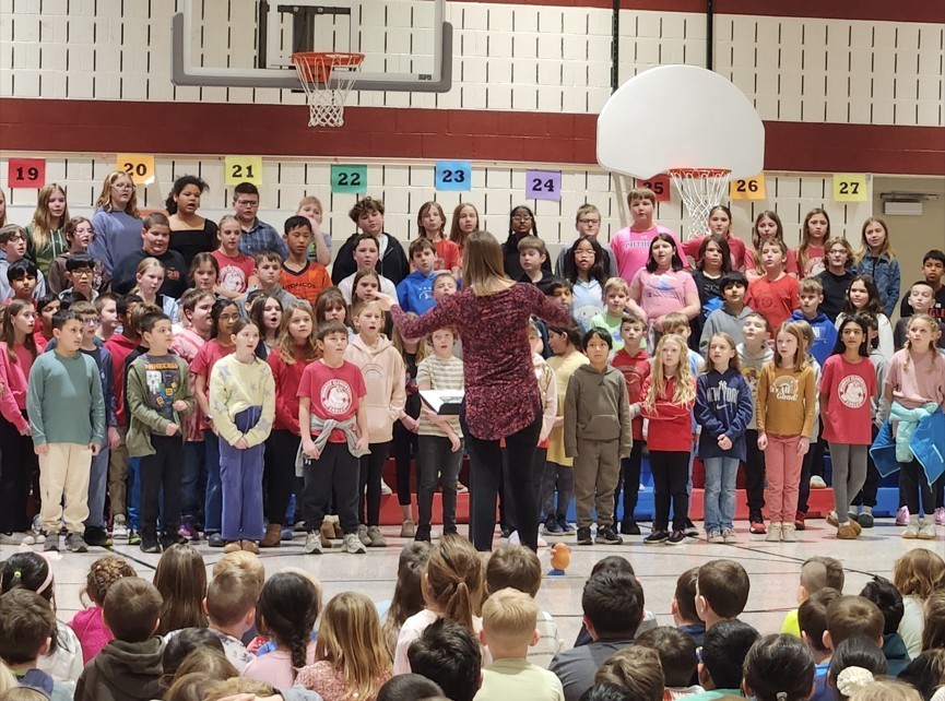 Teacher and students standing in front of other students while singing