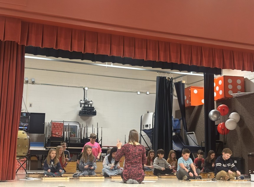Students and teacher sitting on stage practicing instrument