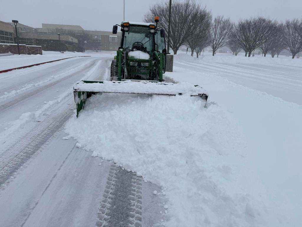 CVSD Maintenance crews plowing snow in the parking lot with a green tractor.