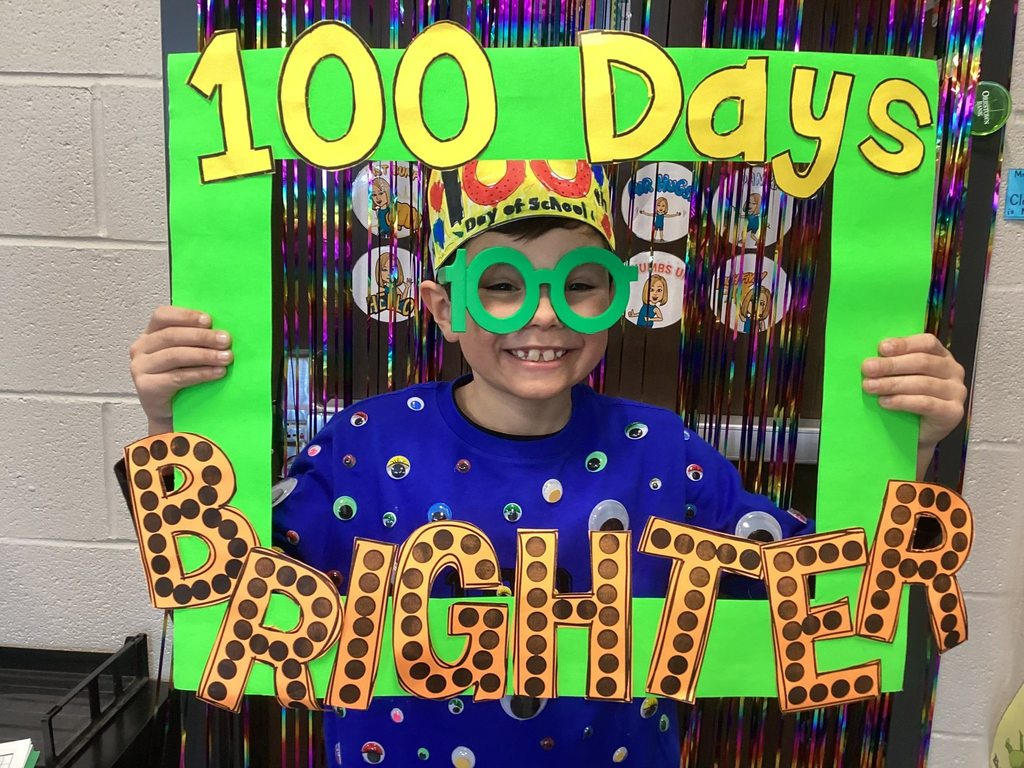 Student holding a colorful frame that reads ‘100 Days Brighter’ to celebrate the 100th day of school.