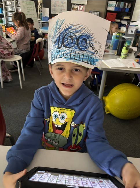 Elementary school-agd boy in blue Sponge Bob sweatshirt with "100 Days Brigther" hand-crafted and colored paper hat.