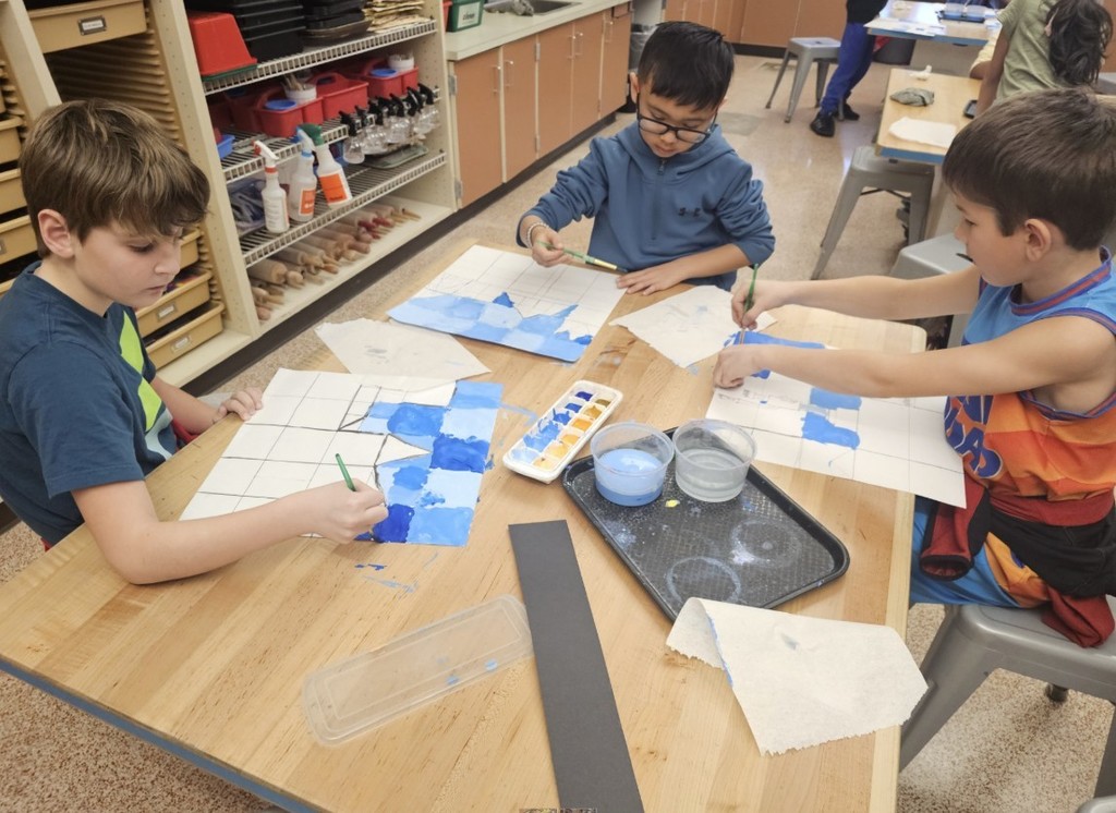 Three third-grade male students painting blue squares during art class.