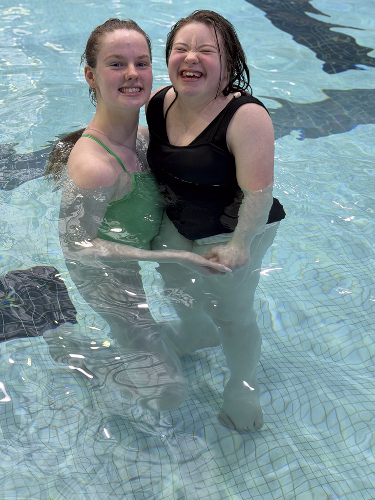 Two people standing together in an indoor pool, holding hands near the shallow end.