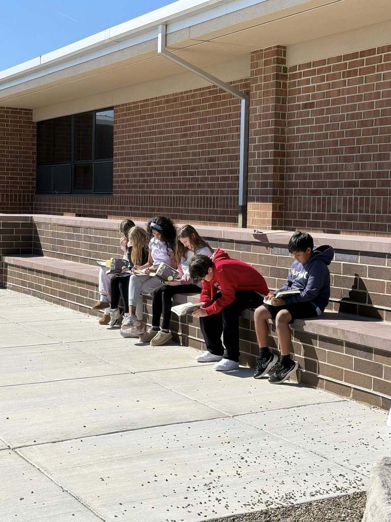 Elementary students sitting in a courtyard, reading books and enjoying the warm weather.