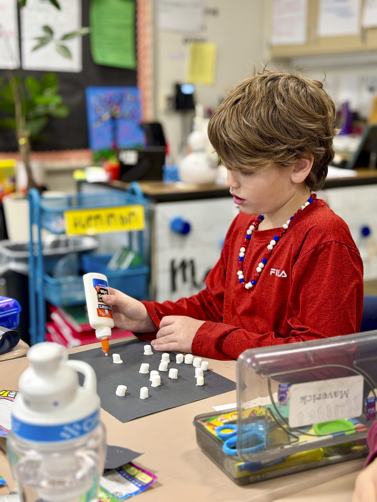 A third-grade student glues mini marshmallows onto black paper to create a constellation during Monroe Elementary’s astronomy unit.