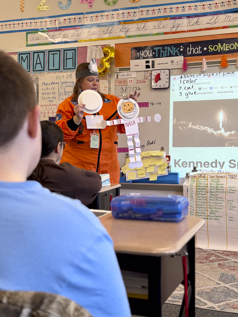 A teacher in an astronaut costume presents a paper astronaut craft to third-grade students during Monroe Elementary’s astronomy unit.