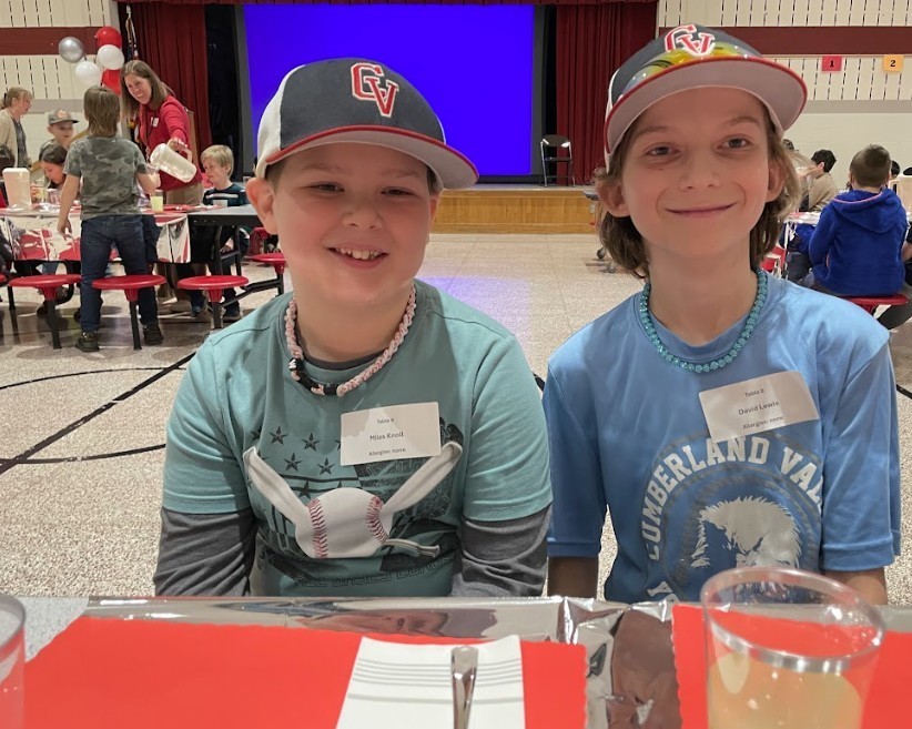 Two male students, both wearing hats and smiling.