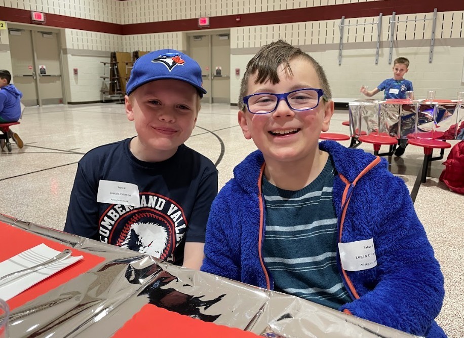 Two male students, one with glasses and the other with a blue hat, smiling happily.