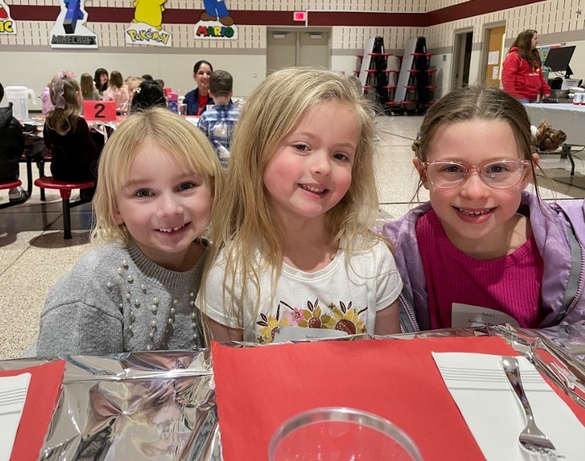 Three young, female students, one wearing glasses; all smiling.
