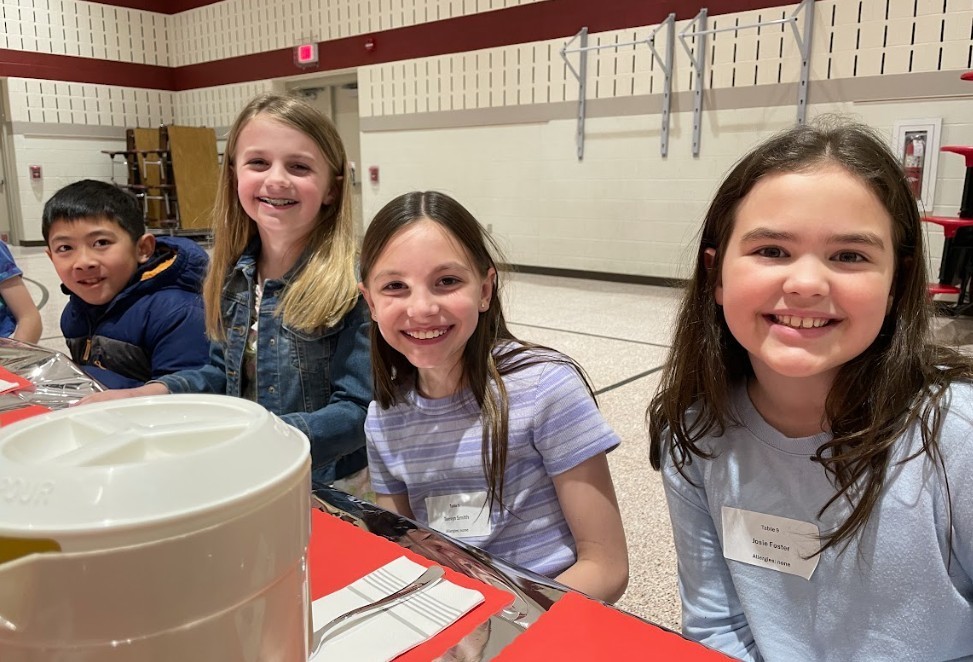 Three female and one male student, smiling happily at the camera.