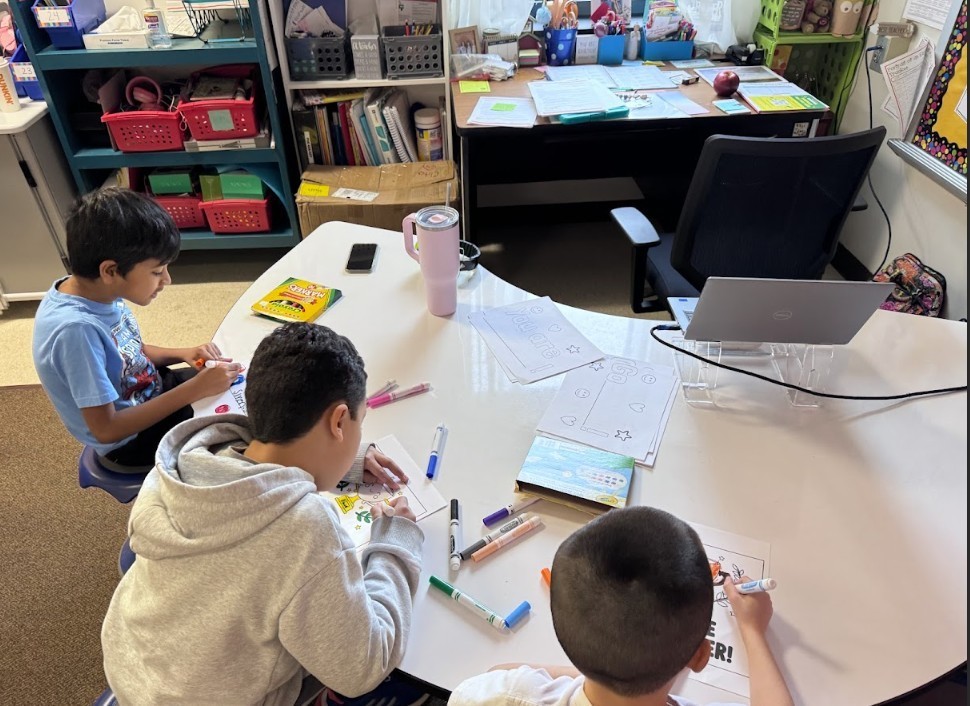 Three boys sitting at kidney table working on encouraging papers