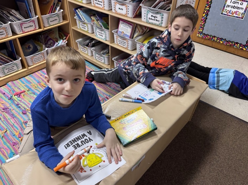 Two boys, one in blue shirt, another in camo shirt, working on papers.