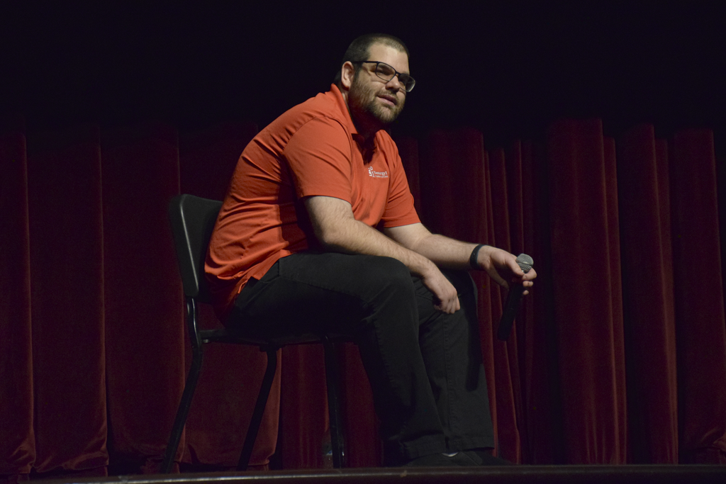 Ben Hartranft sits on a chair on stage as he shares his story with Cumberland Valley staff.