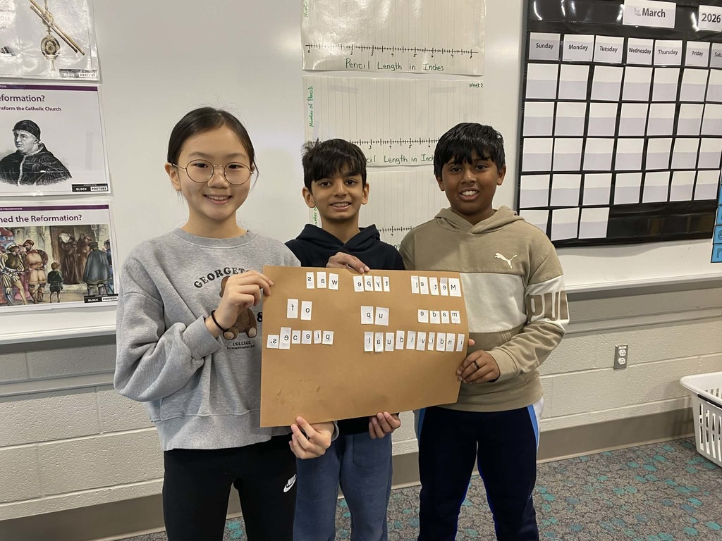 Fifth grade students stand in a classroom holding a board with letter tiles created during a printing press lesson.