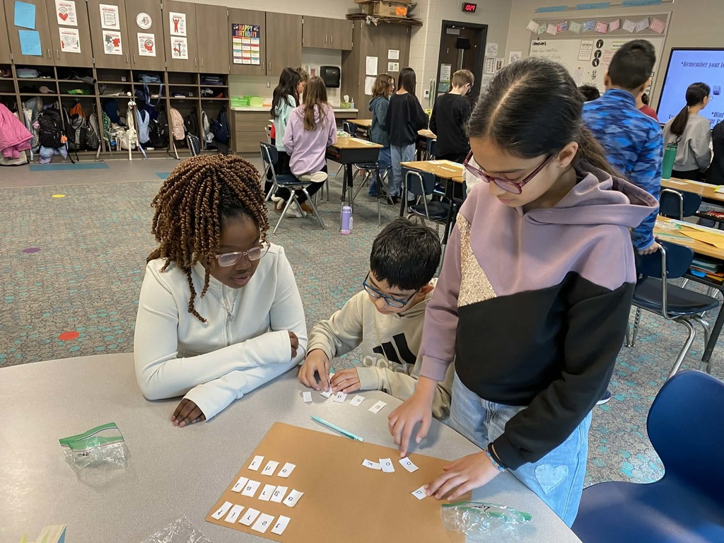 Fifth grade students work together at a classroom table, arranging letter tiles during a lesson about the printing press.