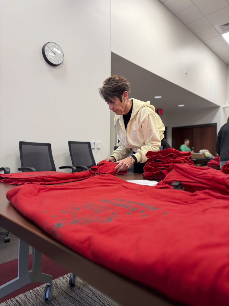 A volunteer folds red athlete shirts for CV's Special Olympics.