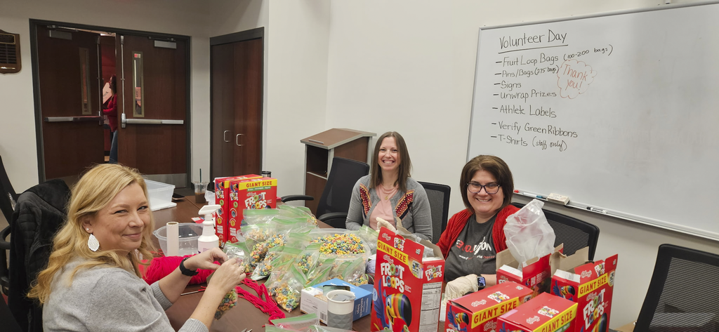 Three volunteers smile as they are prepping snack bags for CV's Special Olympics.