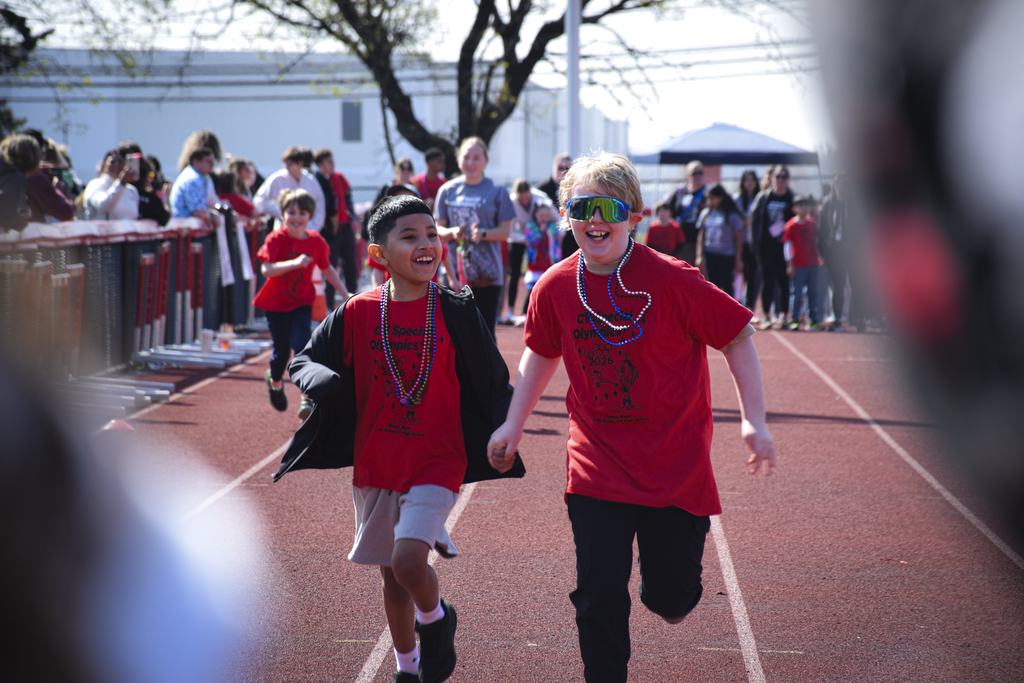 Two students in red shirts run on a track during CV's Special Olympics.