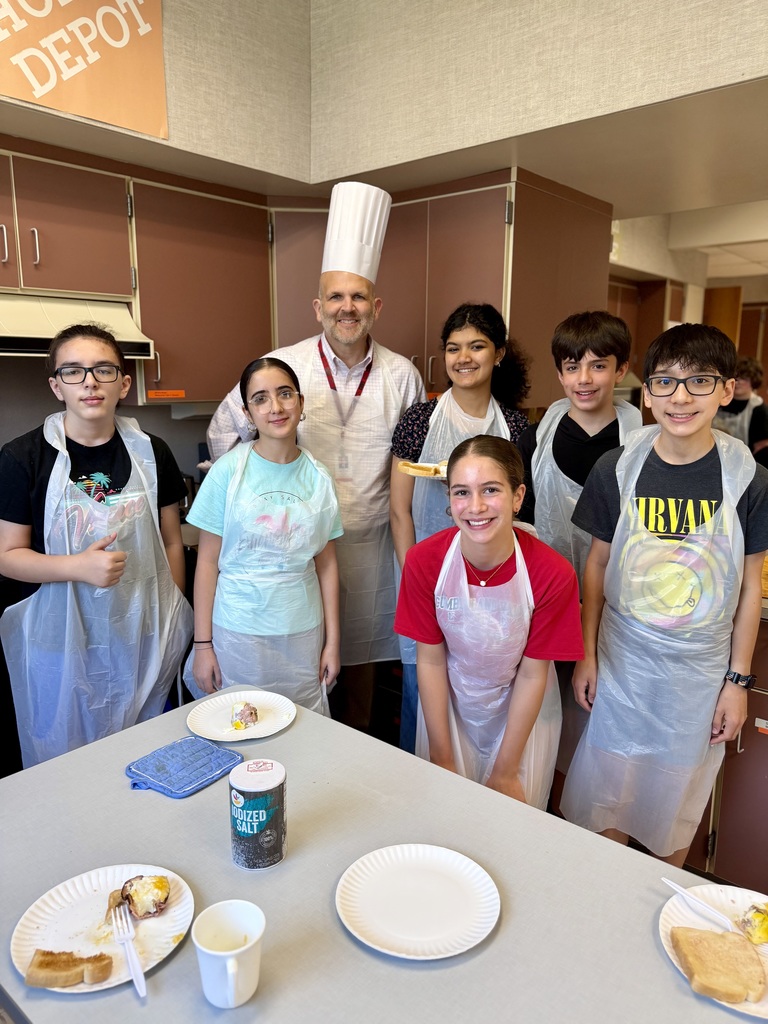 Guest chef, Dr. Blanchard, stands with Eagle View 7th graders during a hands-on cooking class in a school kitchen.