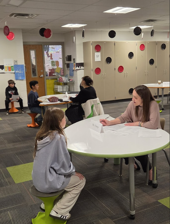 Adult sitting at table with student, writing down information for interview.